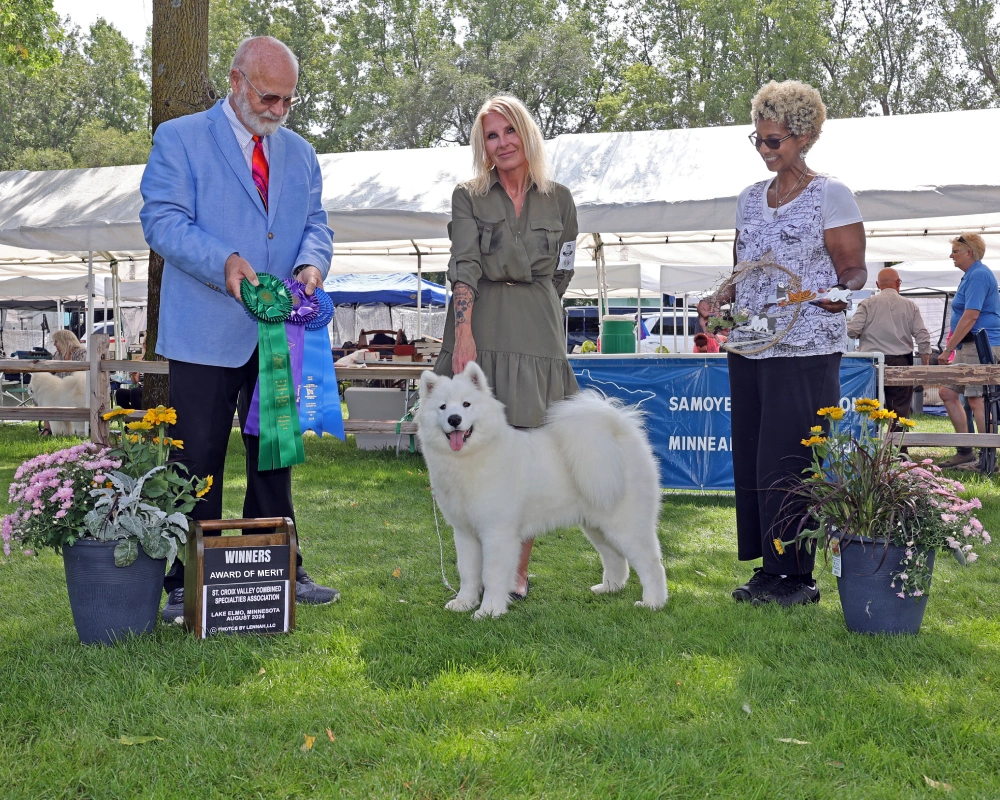 A man and two women standing next to a white dog.