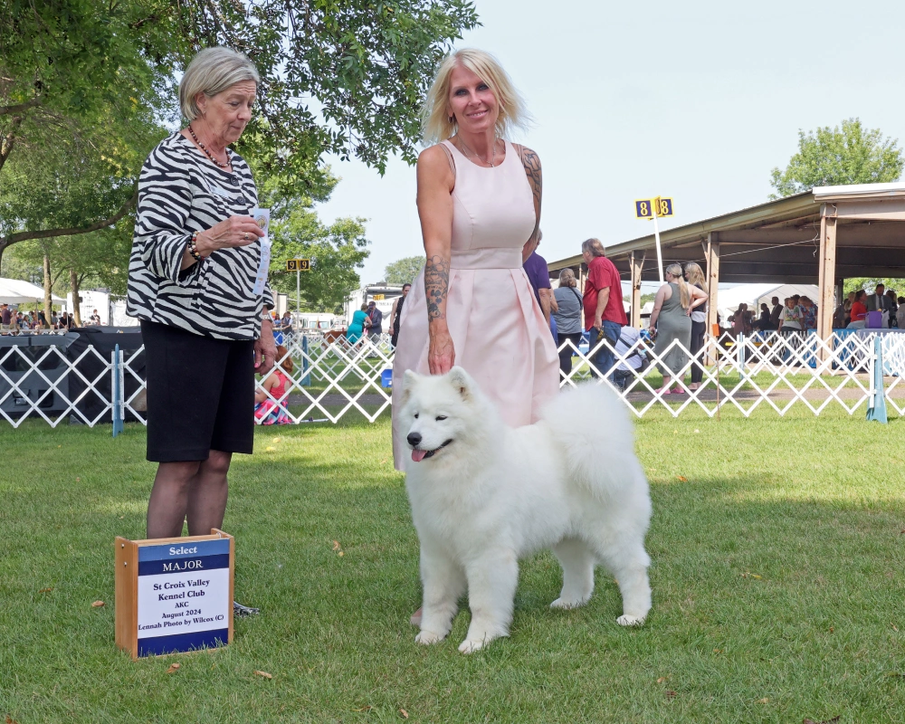 Two women and a white dog standing in the grass.