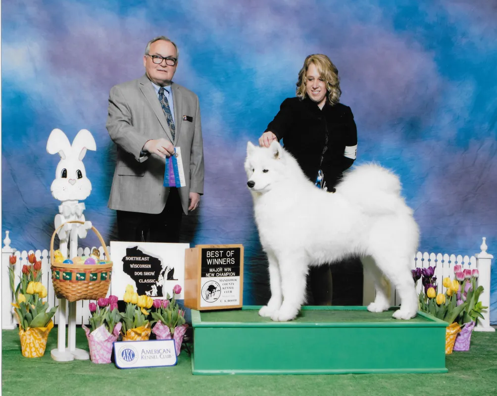 A woman and man standing next to a white dog.